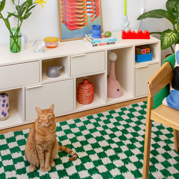 An asymmetrical section Type02 Sideboard in Cotton Beige with mixed open and closed storage stands in front of a chequered rug in a bright kids' room (while a ginger tabby looks on).