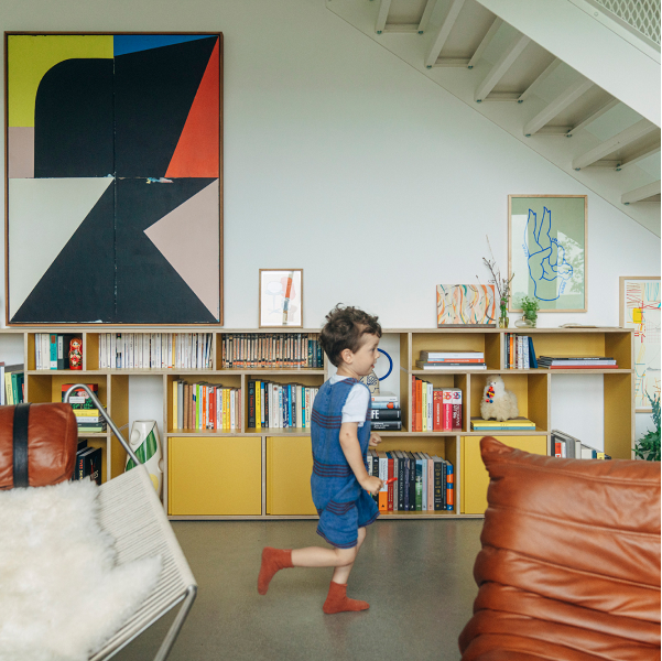 A child sprints past a long, low Type01 Sideboard in Yellow filled with books and decor in a modern, well-decorated room. 