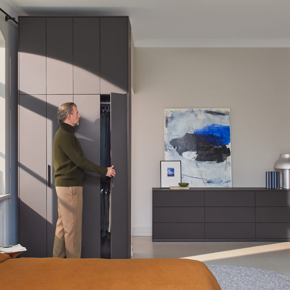An oversized four-door Tone Wardrobe in Graphite Grey with extended top storage stands in a stylish bedroom of dark tones.