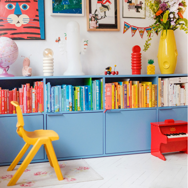 A two-tiered Type02 Sideboard in Sky Blue stands in a colourful children's bedroom and is filled with multicoloured books on the top level and a row of closed doors on the bottom.