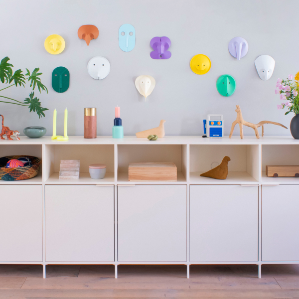 A five-sectioned Type02 Sideboard in Cotton Beige with slim legs and a row of doors topped with open sections displays colourful objects in a children's room with a mauve wall.