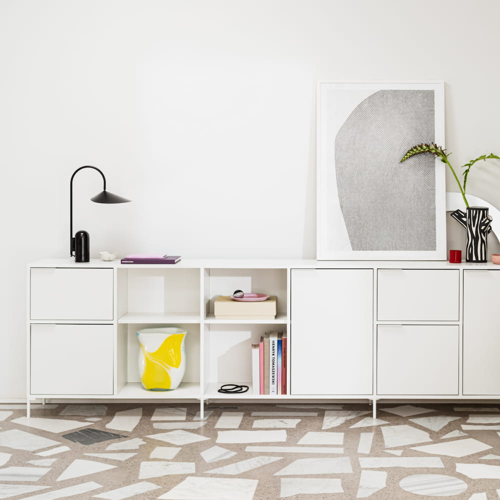 A sleek Type02 Sideboard in white with mixed rows of doors, drawers and open sections stands artfully decorated in a bright living room.