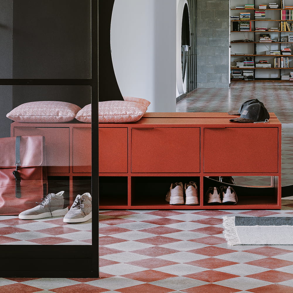 A bold red Type02 Shoe Rack with stacked closed door storage on top of four open sections stands in a hallway with a chequered red and white floor.