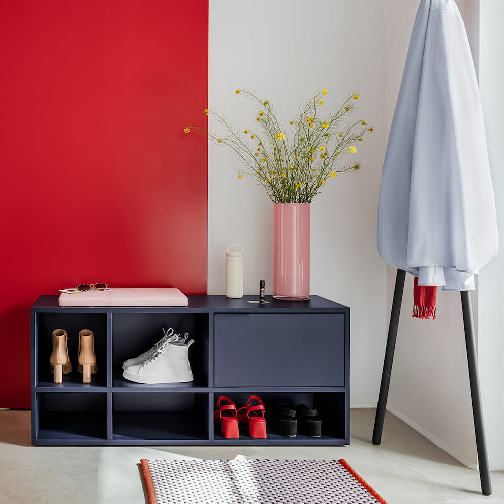 A petite two-row Type02 Shoe Rack in Midnight Blue with one drawer and five open sections of various sizes holds two pairs of white and red shoes in a colourful hallway.