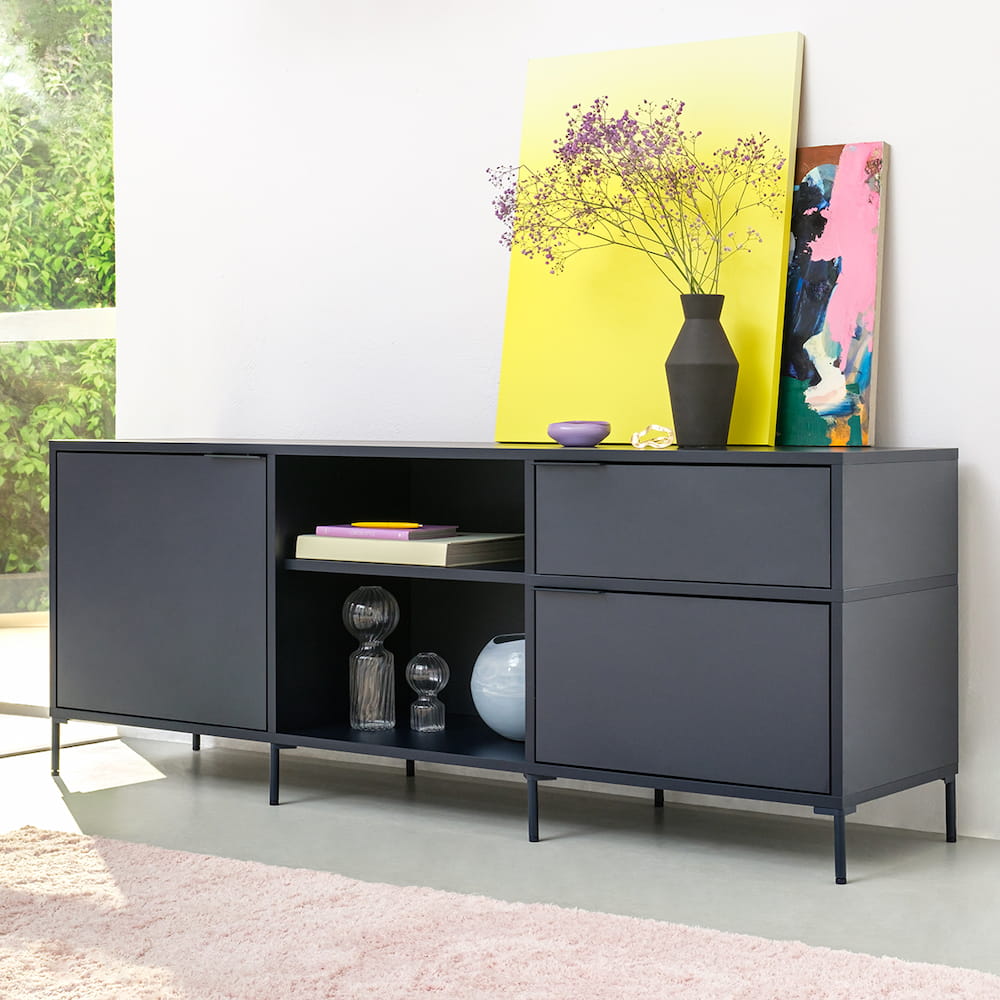 A cool Midnight Blue Type02 Sideboard with legs stands at an angle in a living room showing off two rows of drawers divided by a middle open section stacked with books.
