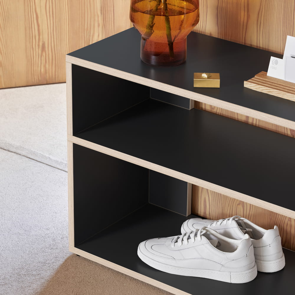 A simple, stylish black Type01 Shoe Rack with contrasting wood edges holds a pair of white shoes in one of two open rows in a modern hallway.