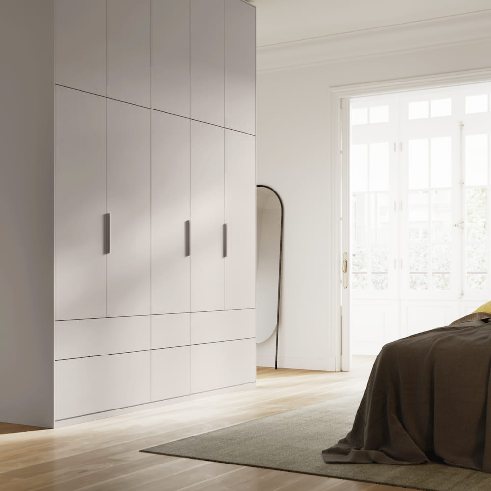 A sleek, tall Tone Wardrobe in White, with five slim doors and external lower drawers, plus added top storage, stands in a tranquil bedroom.